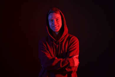 Photo of Portrait of smiling man wearing hoodie with crossed arms in neon lights against black background