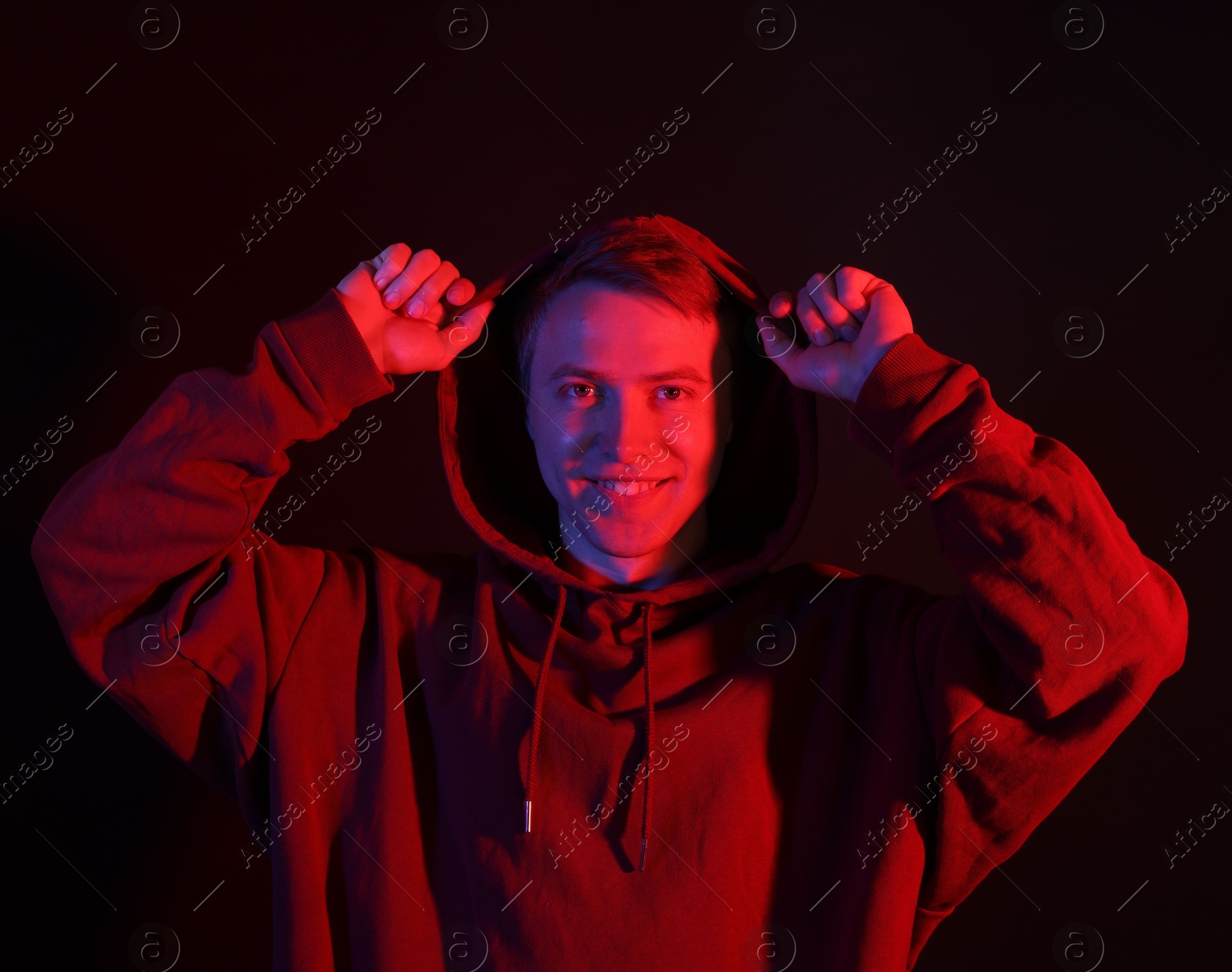 Portrait of smiling man wearing hoodie with crossed arms in neon lights against black background Photo of Portrait of smiling man wearing hoodie with crossed arms in neon lights against black background