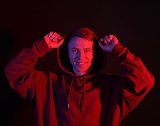 Photo of Portrait of smiling man wearing hoodie with crossed arms in neon lights against black background
