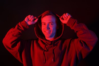 Photo of Portrait of smiling man wearing hoodie with crossed arms in neon lights against black background