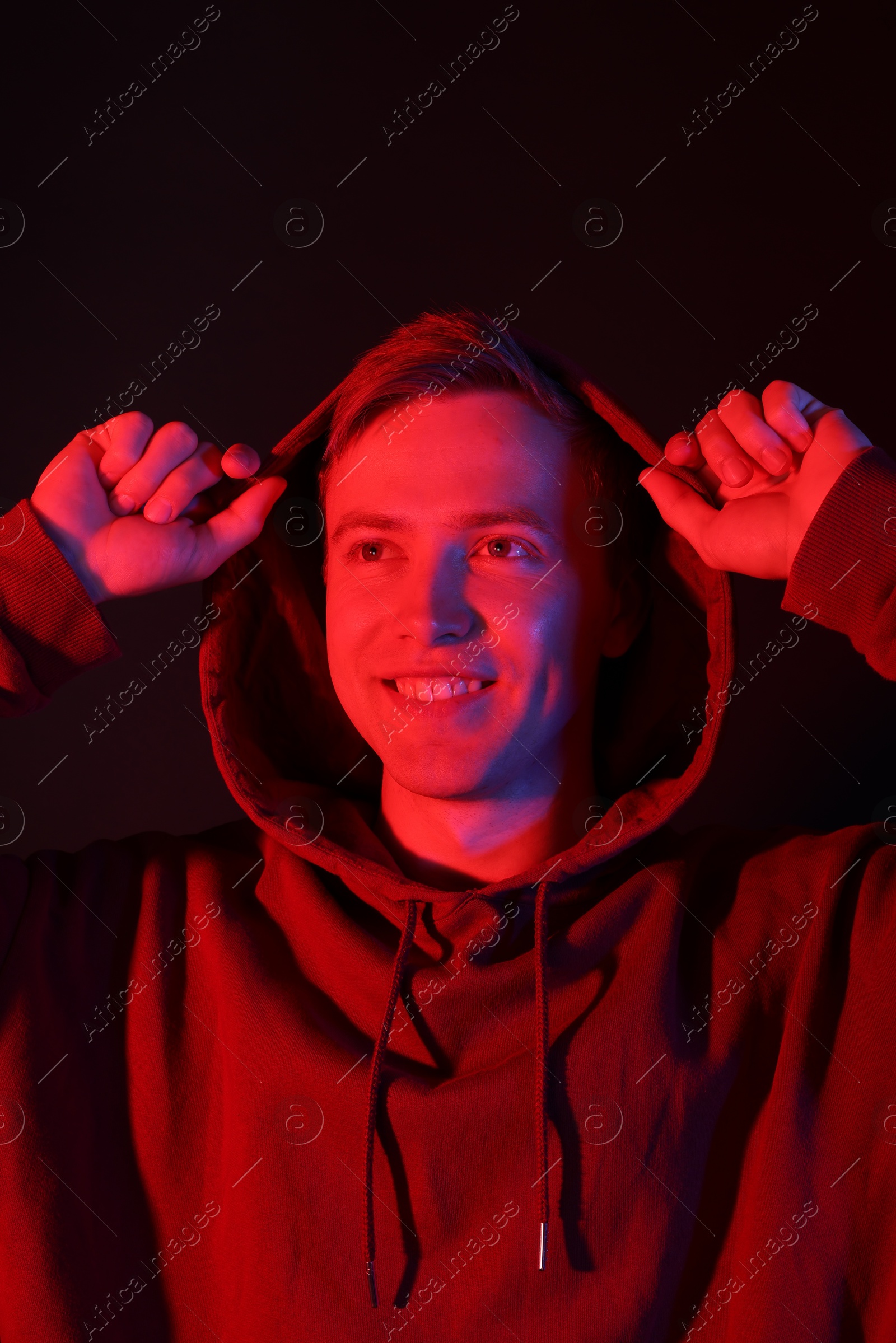 Smiling man wearing hoodie in neon lights against black background Photo of Smiling man wearing hoodie in neon lights against black background