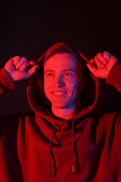 Photo of Smiling man wearing hoodie in neon lights against black background
