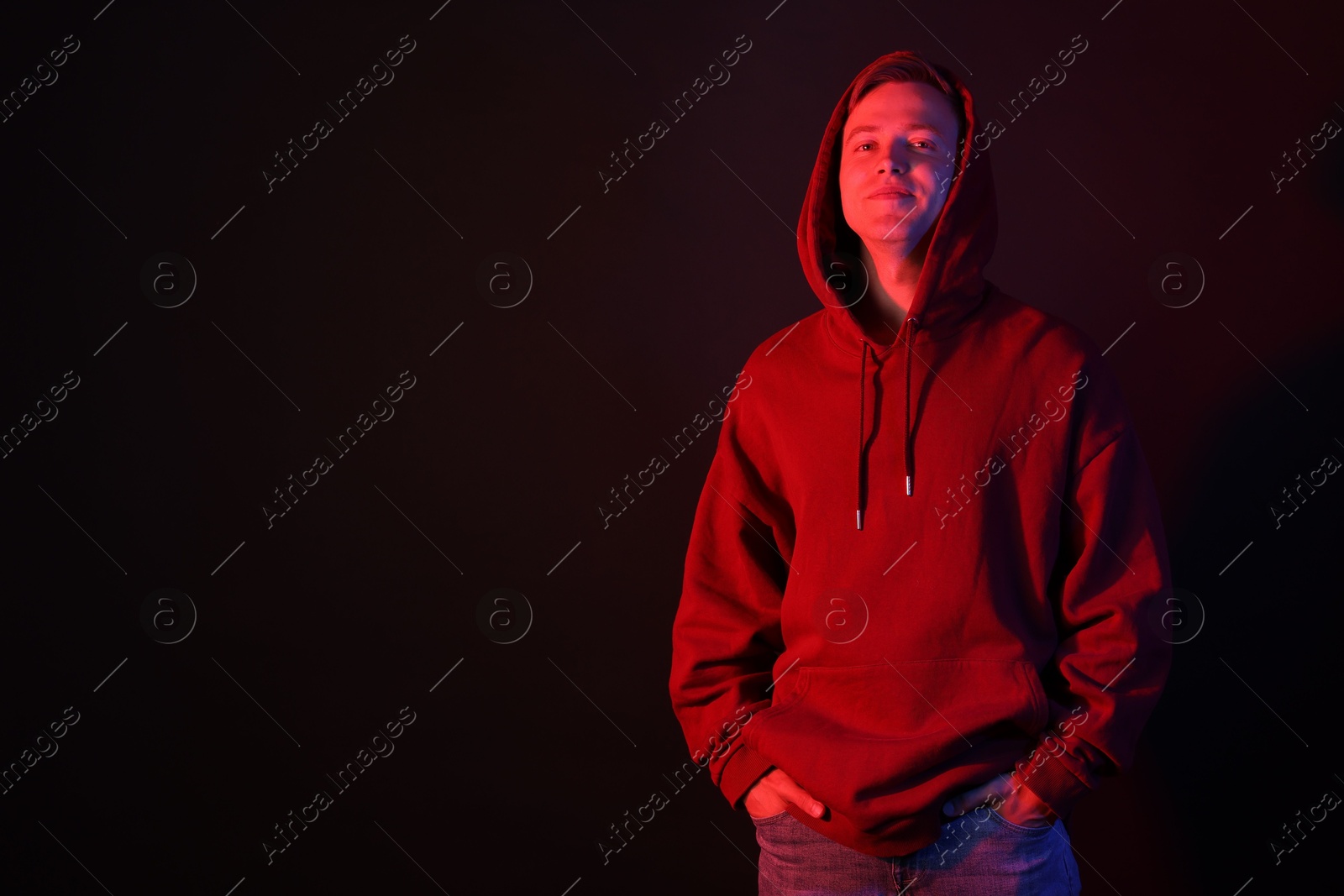 Photo of Handsome man wearing hoodie in neon lights against black background. Space for text