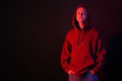 Photo of Handsome man wearing hoodie in neon lights against black background. Space for text