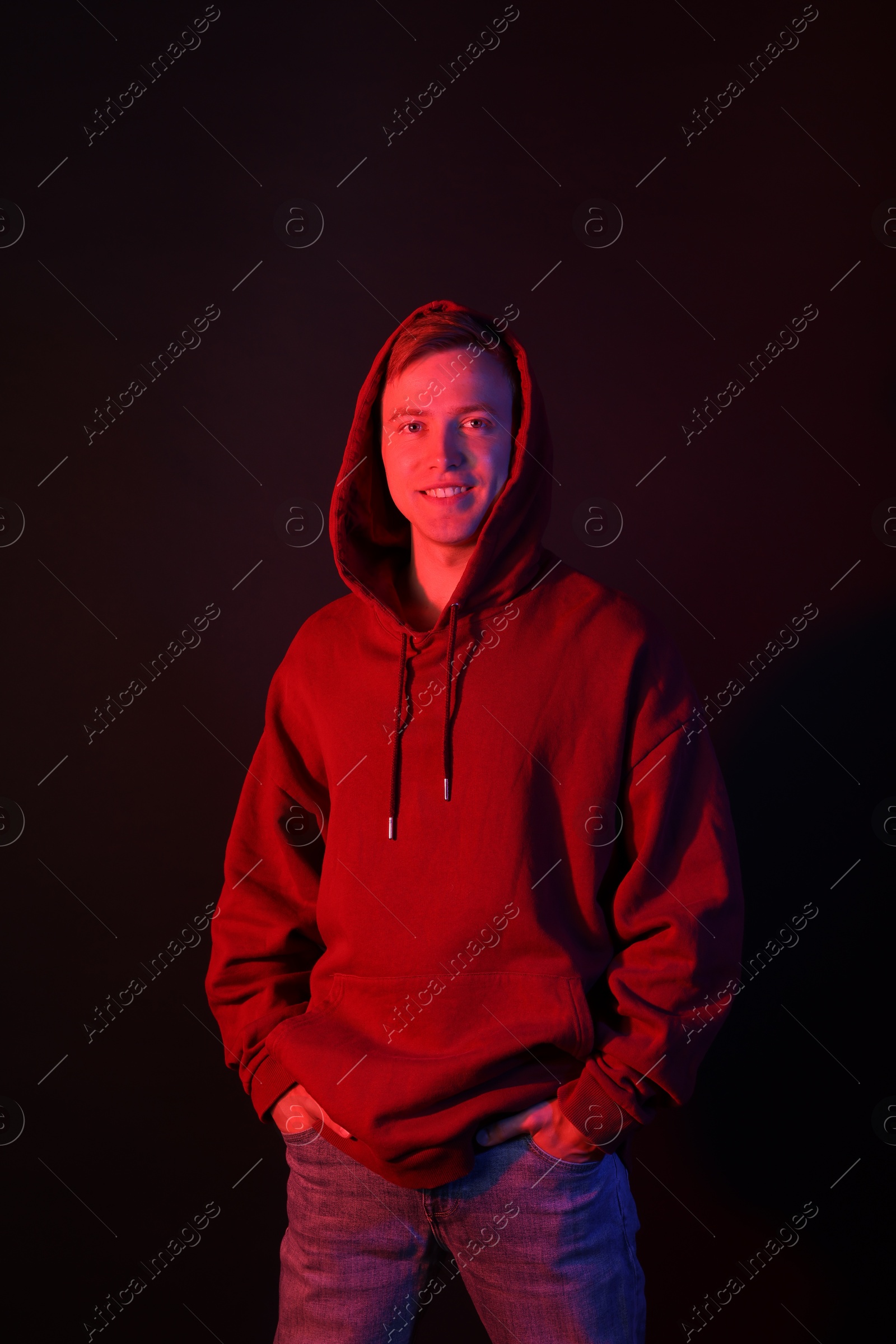Photo of Portrait of smiling man wearing hoodie in neon lights against black background