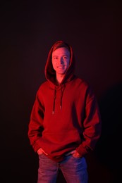 Photo of Portrait of smiling man wearing hoodie in neon lights against black background
