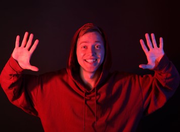Photo of Portrait of smiling man wearing hoodie in neon lights against black background