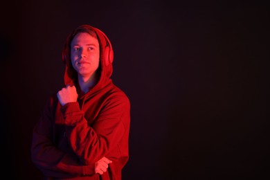 Photo of Handsome man wearing hoodie and headphones in neon lights against black background. Space for text