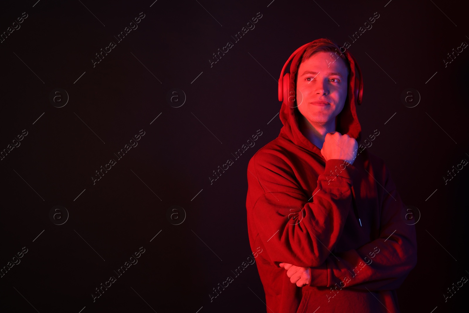 Handsome man wearing hoodie and headphones in neon lights against black background. Space for text Photo of Handsome man wearing hoodie and headphones in neon lights against black background. Space for text