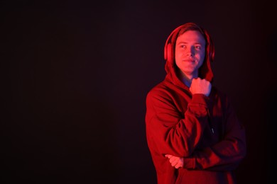 Photo of Handsome man wearing hoodie and headphones in neon lights against black background. Space for text