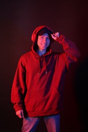 Photo of Portrait of smiling man wearing hoodie, baseball cap and headphones in neon lights against black background