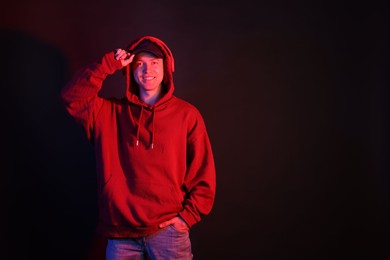 Photo of Smiling man wearing hoodie, baseball cap and headphones in neon lights against black background. Space for text