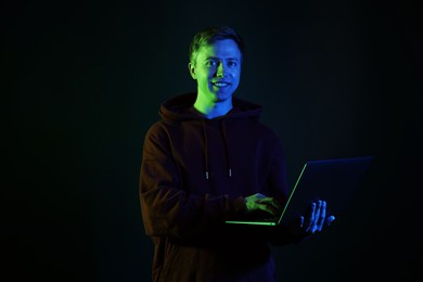 Photo of Smiling man wearing hoodie using laptop in neon lights against black background