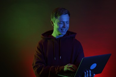 Photo of Smiling man wearing hoodie using laptop in neon lights against black background