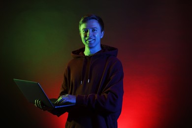Photo of Smiling man wearing hoodie using laptop in neon lights against black background