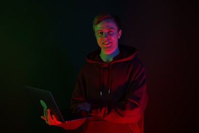 Photo of Smiling man wearing hoodie using laptop in neon lights against black background