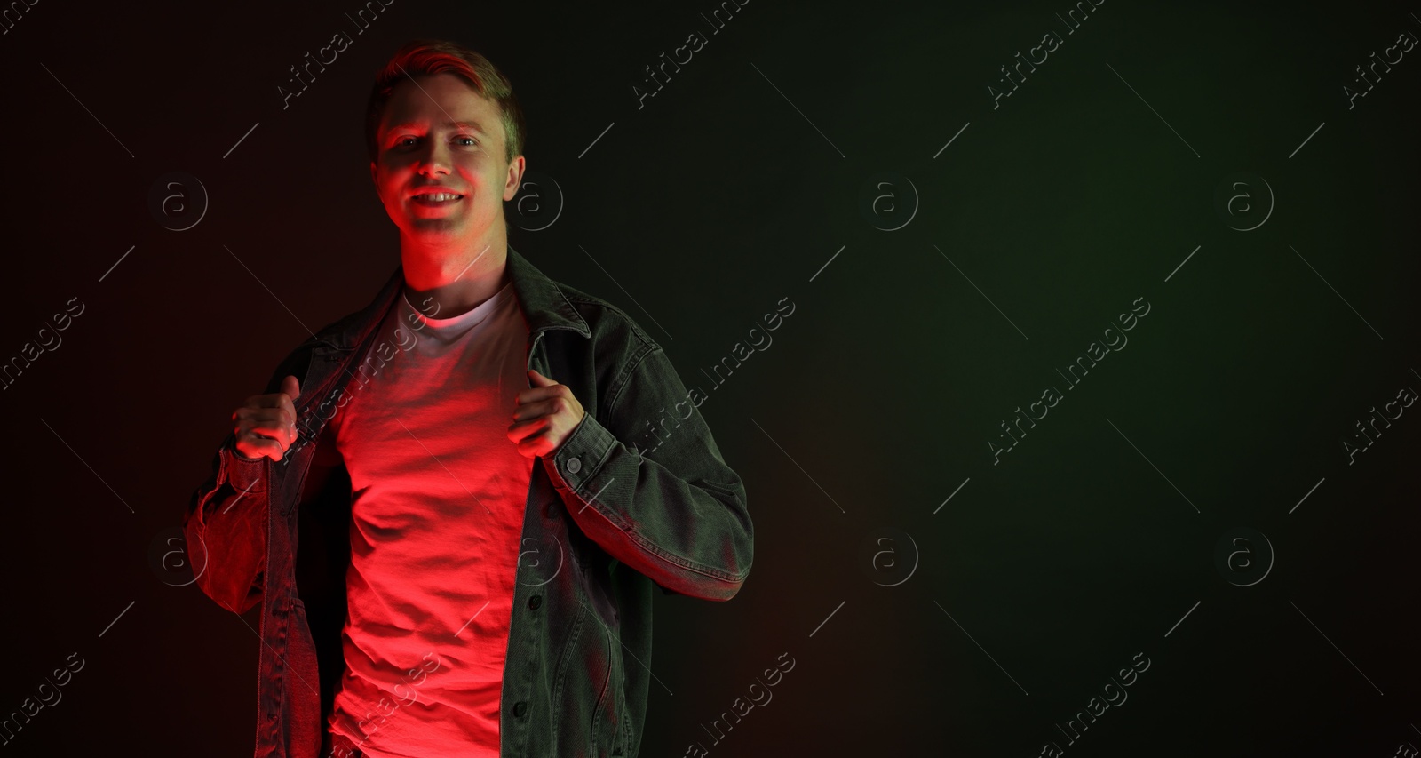 Portrait of smiling man wearing jacket in neon lights against black background. Space for text Photo of Portrait of smiling man wearing jacket in neon lights against black background. Space for text