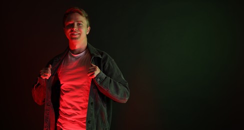 Photo of Portrait of smiling man wearing jacket in neon lights against black background. Space for text