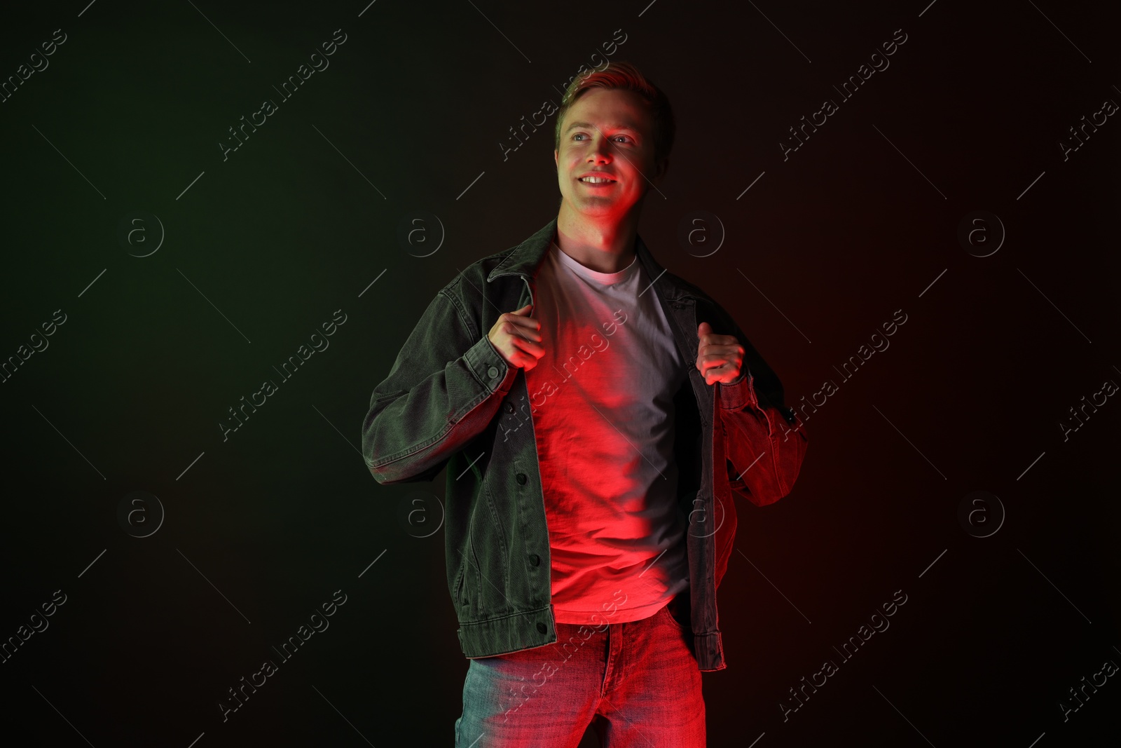Smiling man wearing jacket in neon lights against black background Photo of Smiling man wearing jacket in neon lights against black background