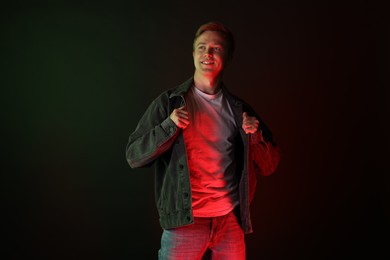 Photo of Smiling man wearing jacket in neon lights against black background