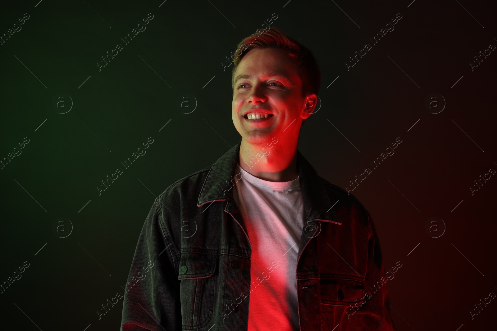Smiling man wearing jacket in neon lights against black background Photo of Smiling man wearing jacket in neon lights against black background