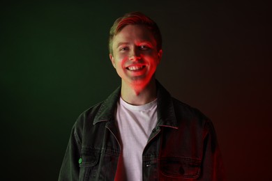 Photo of Portrait of smiling man wearing jacket in neon lights against black background