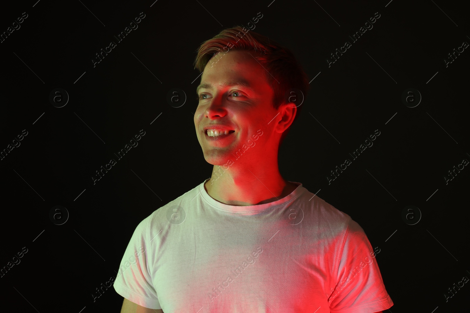 Smiling man in neon lights against black background Photo of Smiling man in neon lights against black background