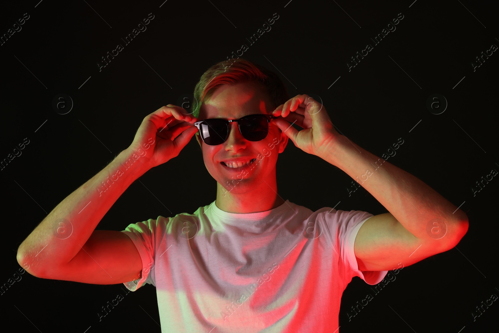 Smiling man wearing sunglasses in neon lights against black background Photo of Smiling man wearing sunglasses in neon lights against black background
