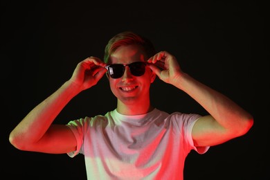 Photo of Smiling man wearing sunglasses in neon lights against black background