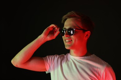 Photo of Smiling man wearing sunglasses in neon lights against black background