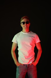 Photo of Smiling man wearing sunglasses in neon lights against black background