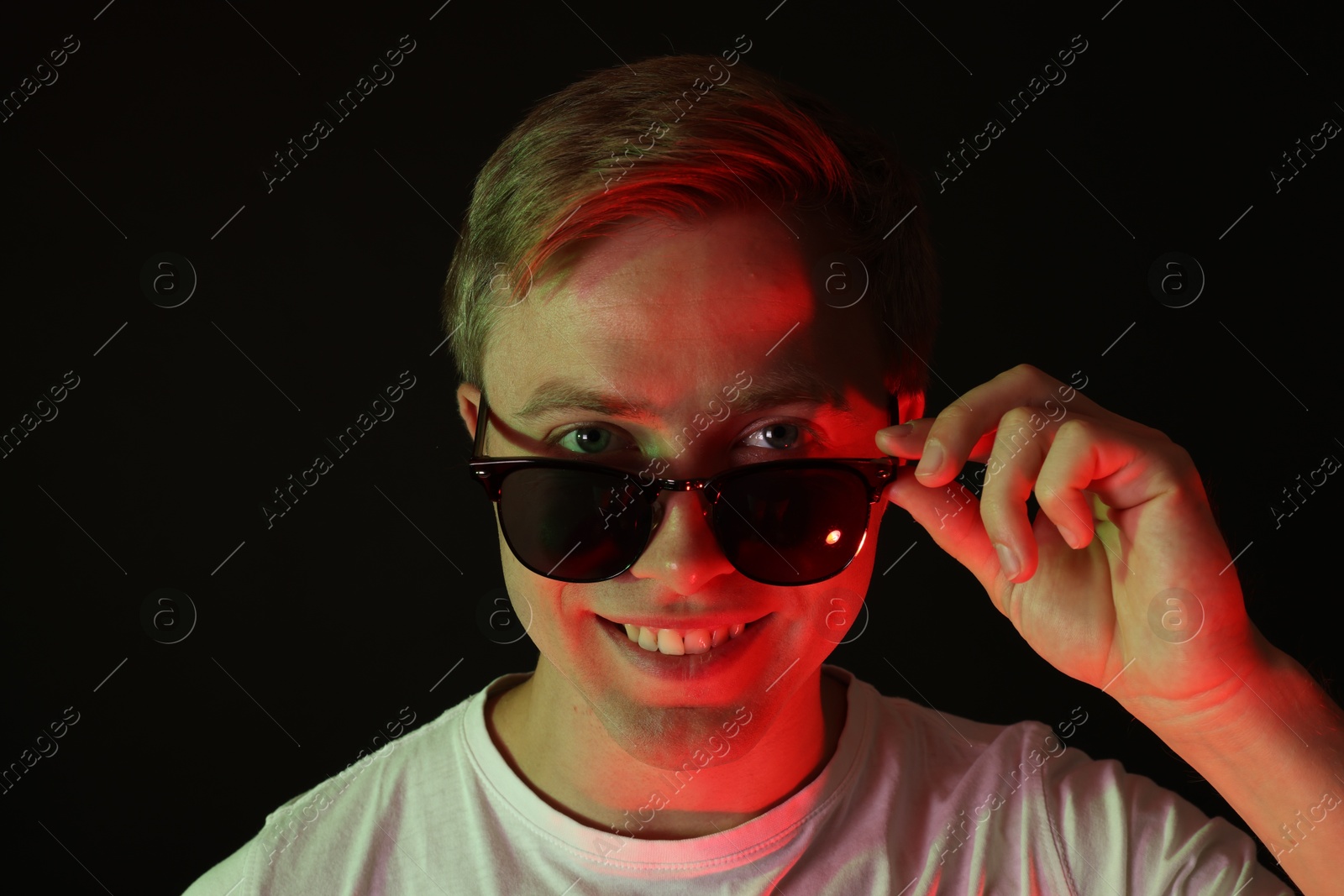 Photo of Portrait of smiling man wearing sunglasses in neon lights against black background