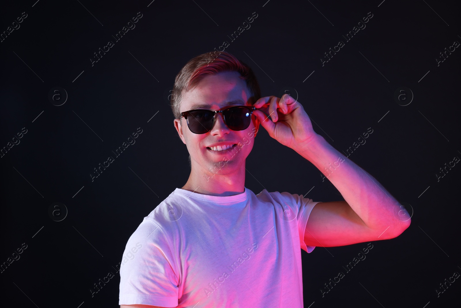 Smiling man wearing sunglasses in neon lights against black background Photo of Smiling man wearing sunglasses in neon lights against black background