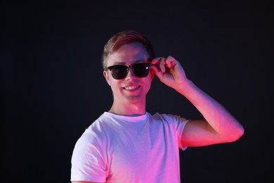 Photo of Smiling man wearing sunglasses in neon lights against black background