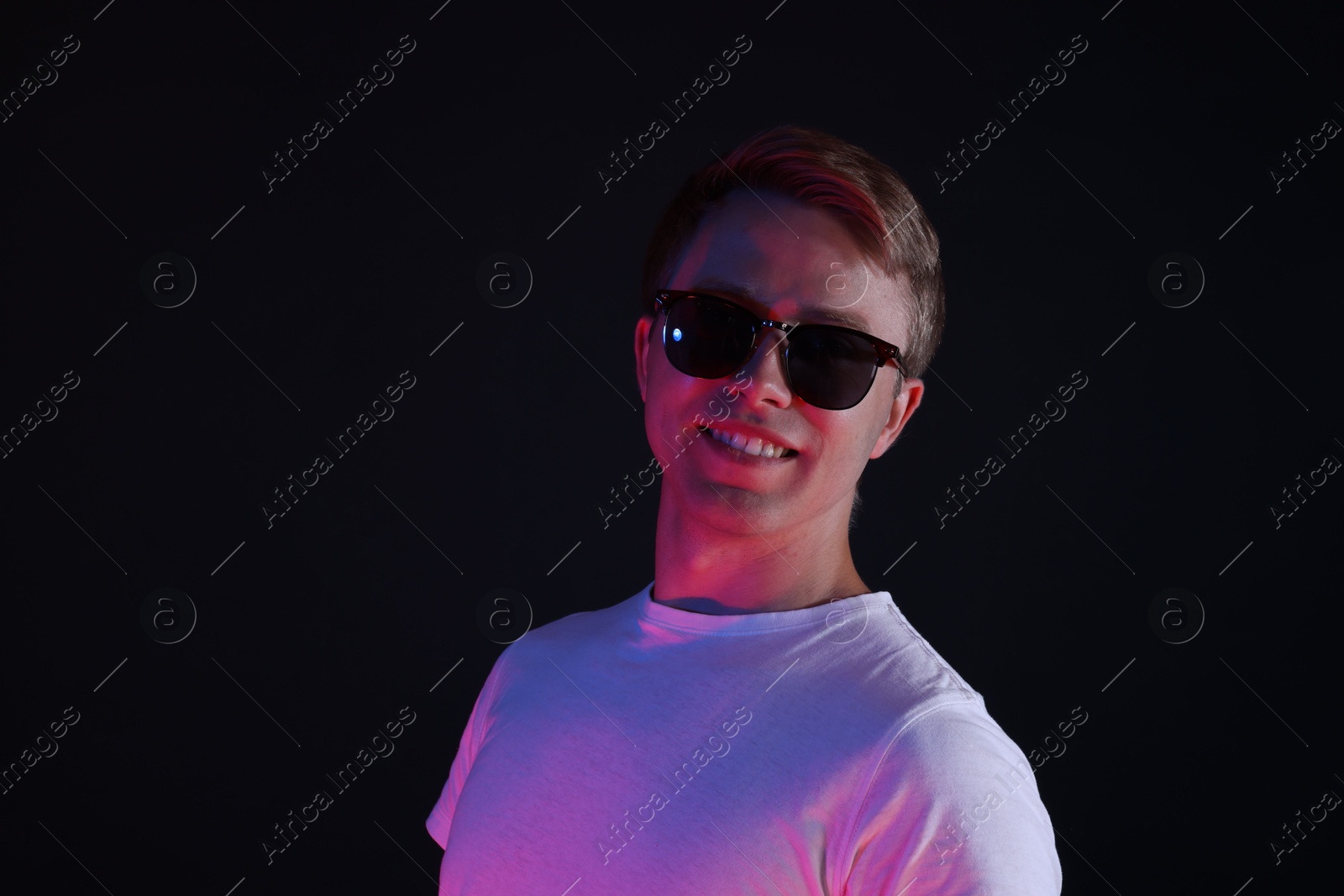 Smiling man wearing sunglasses in neon lights against black background Photo of Smiling man wearing sunglasses in neon lights against black background