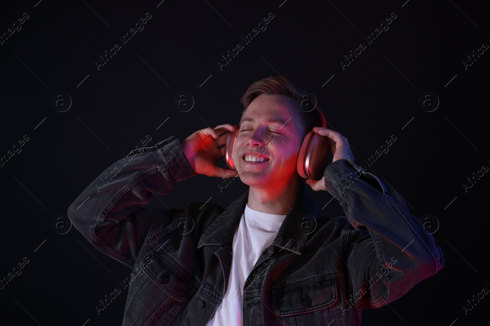 Smiling man wearing headphones listening to music in neon lights against black background Photo of Smiling man wearing headphones listening to music in neon lights against black background