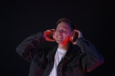 Photo of Smiling man wearing headphones listening to music in neon lights against black background