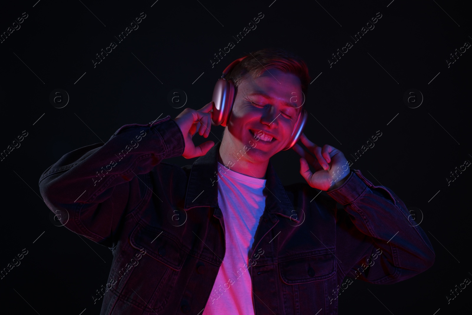 Smiling man wearing headphones listening to music in neon lights against black background Photo of Smiling man wearing headphones listening to music in neon lights against black background