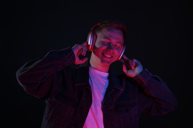 Photo of Smiling man wearing headphones listening to music in neon lights against black background
