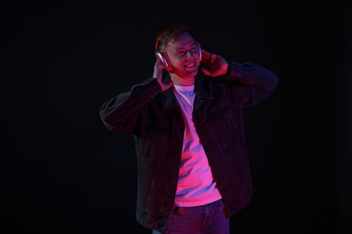 Photo of Smiling man wearing headphones listening to music in neon lights against black background