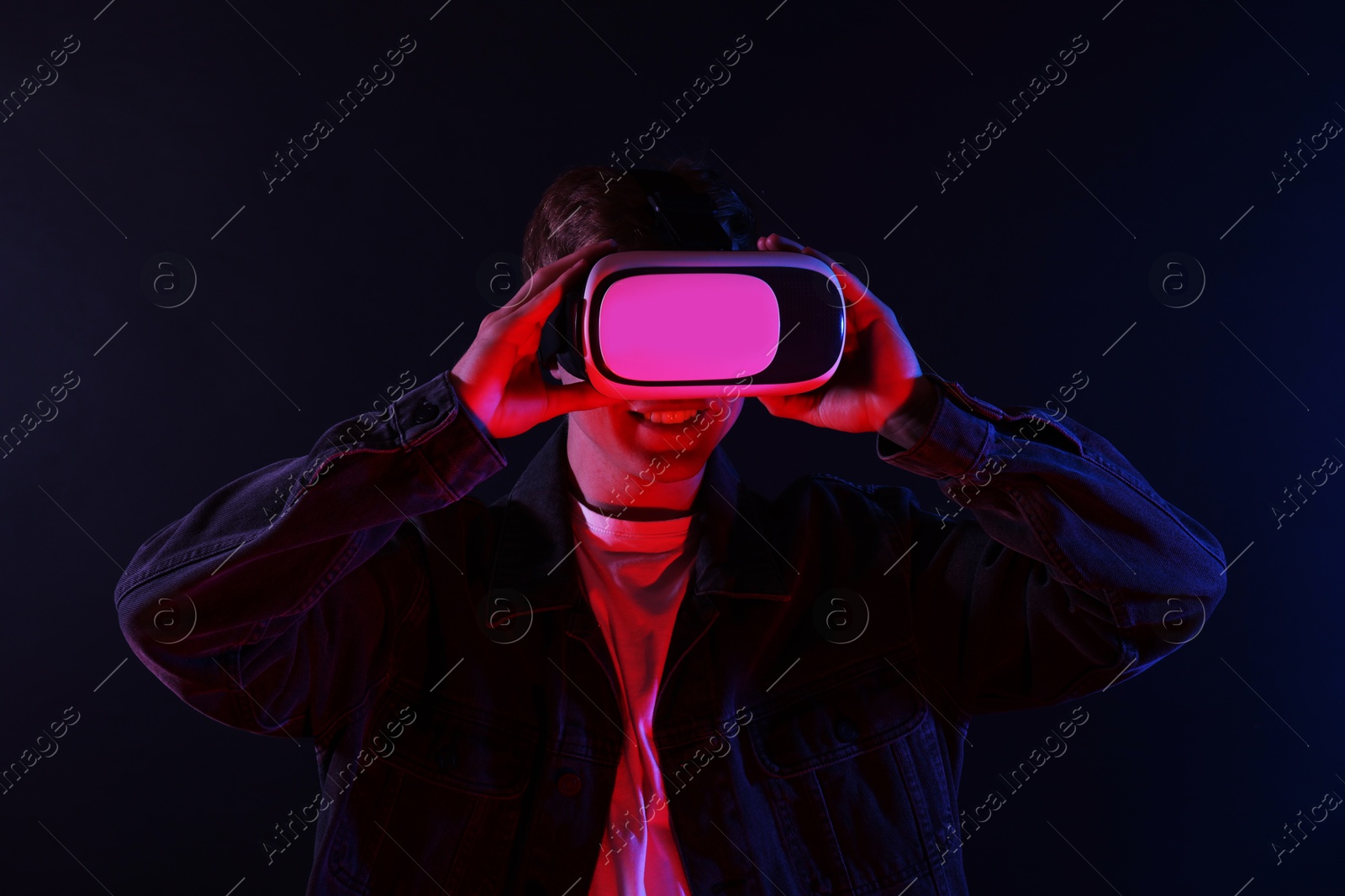 Smiling man using virtual reality headset in neon lights against black background Photo of Smiling man using virtual reality headset in neon lights against black background