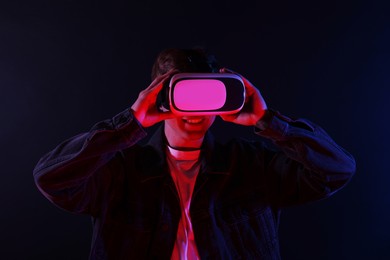 Photo of Smiling man using virtual reality headset in neon lights against black background