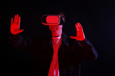 Photo of Smiling man using virtual reality headset in neon lights against black background
