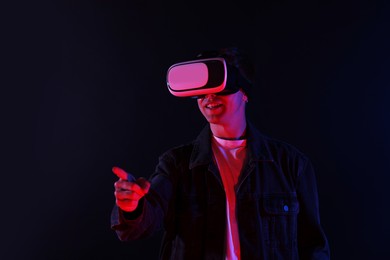 Photo of Smiling man using virtual reality headset in neon lights against black background