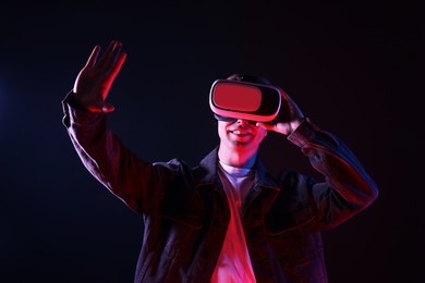 Photo of Smiling man using virtual reality headset in neon lights against black background