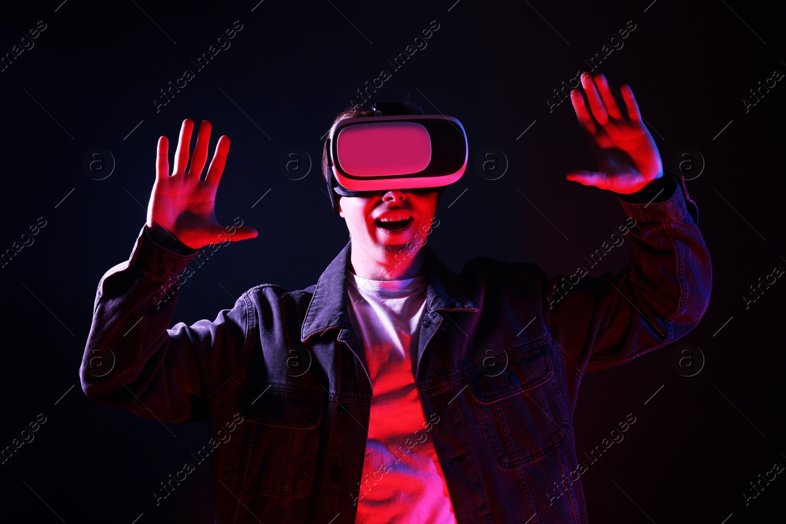 Emotional man using virtual reality headset in neon lights against black background Photo of Emotional man using virtual reality headset in neon lights against black background