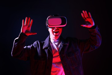 Photo of Emotional man using virtual reality headset in neon lights against black background