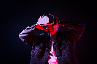 Photo of Smiling man using virtual reality headset in neon lights against black background