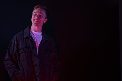 Photo of Smiling man in neon lights against black background. Space for text