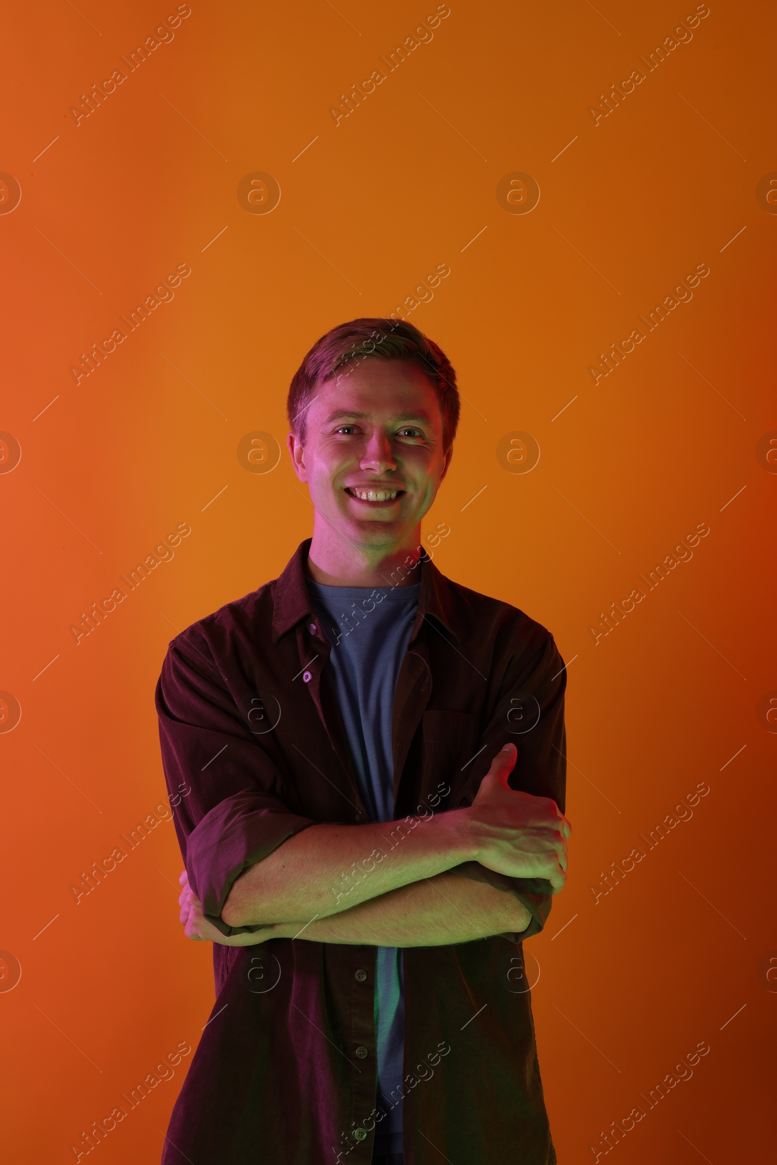 Portrait of smiling man in neon lights against orange background Photo of Portrait of smiling man in neon lights against orange background